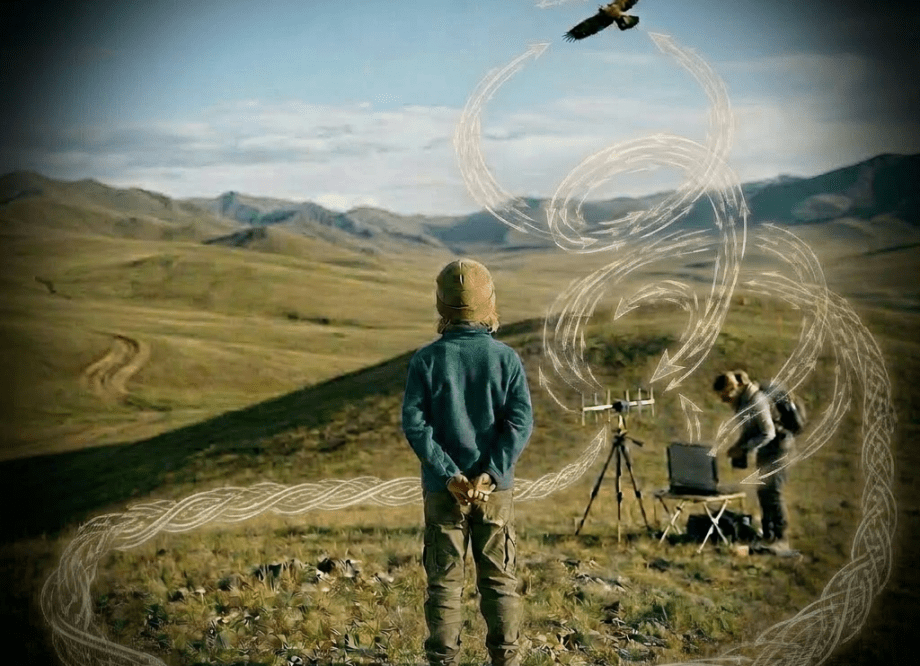 Child shading eyes looking at bird flying above grassy hills with adult setting up equipment